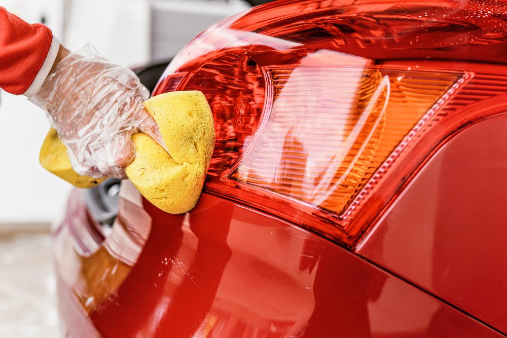 young woman cleaning rear lights her car closeup detail hand glove holding yellow sponge